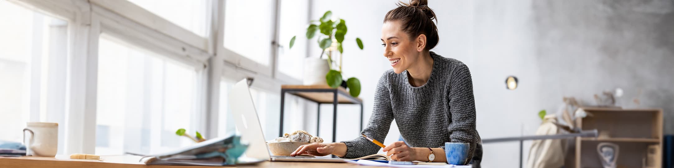 eine junge Frau arbeitet an einem Laptop und hält einen Stift in der Hand